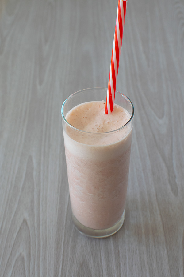 Pink smoothie in a clear glass with a red and white straw on a white wood table