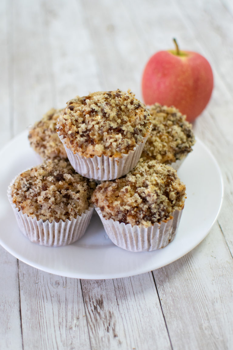 Easy Dairy-Free Apple Cinnamon Muffins piled on a white plate next to a red apple