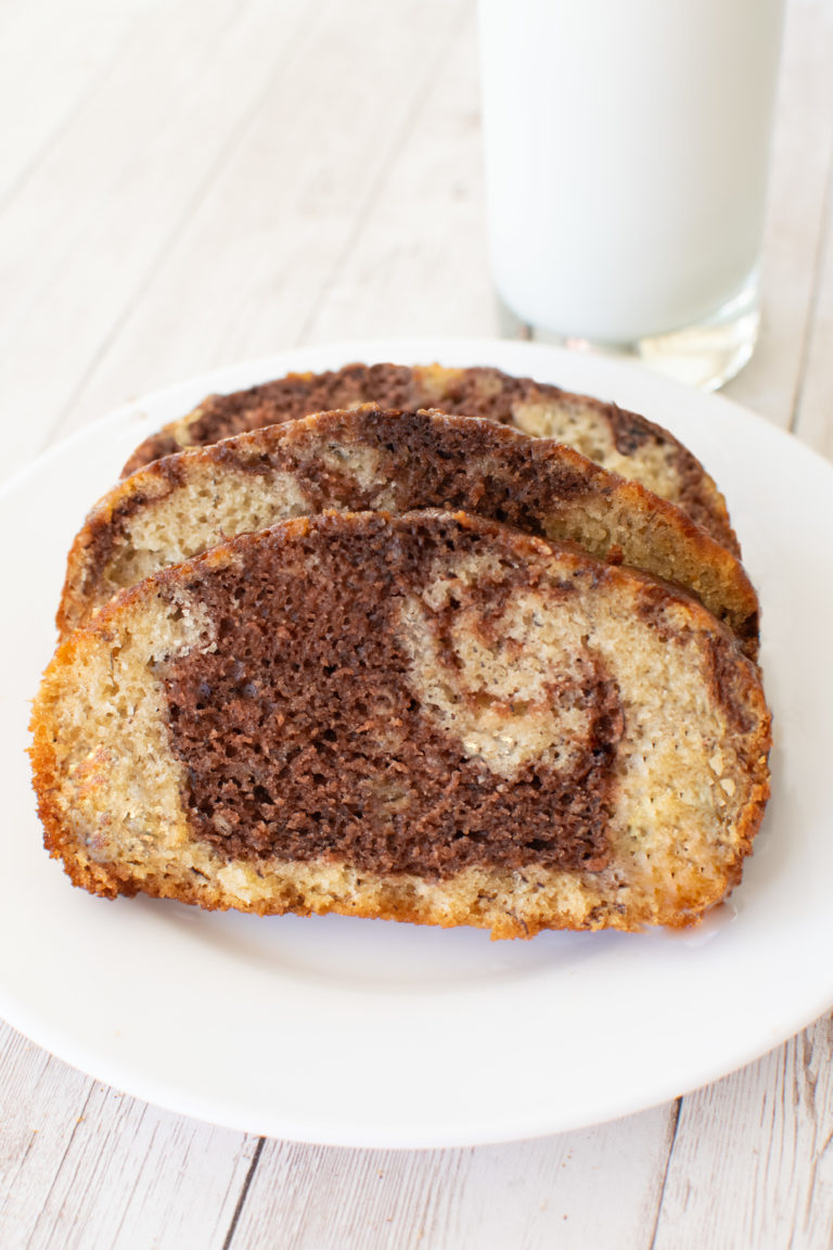 Slices of Easy Chocolate Banana Marble Cake on a white plate near a glass of milk on a white wood table