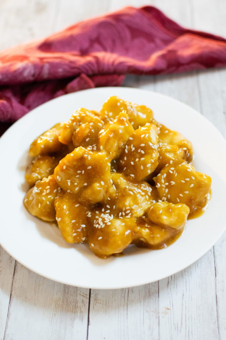kosher honey garlic chicken on a white plate with a red cloth napkin nearby on a white wood table