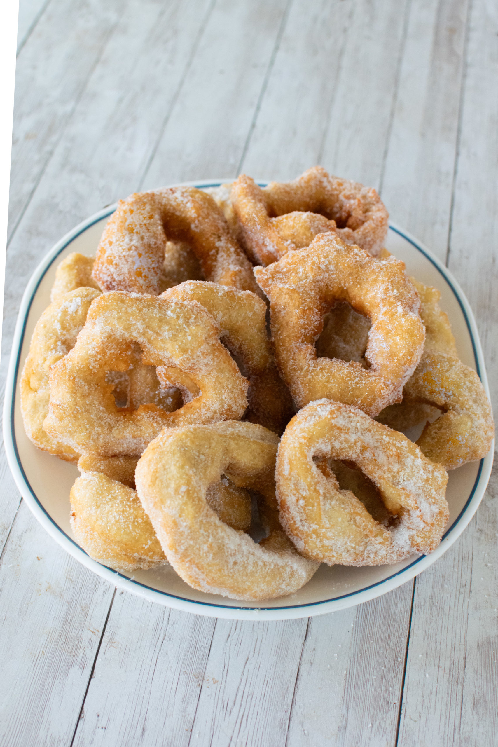 Easy moroccan doughnuts (sfinge) on a white plate with a blue rim on a white wood background.