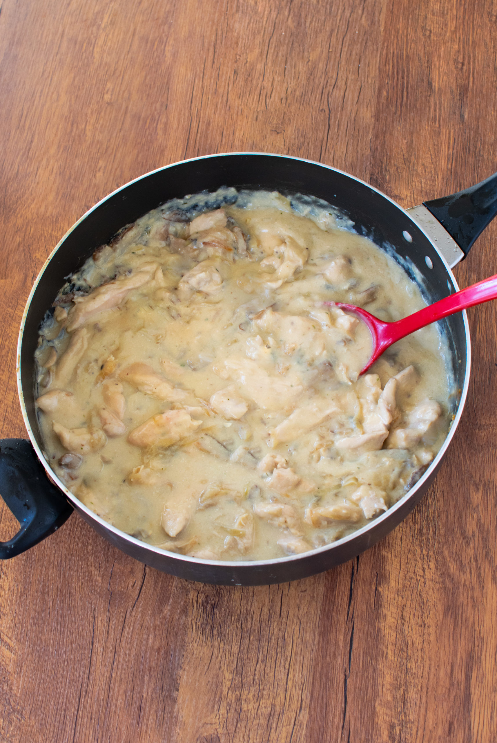 dairy-free chicken stroganoff in a pan with a red serving spoon on a dark wood table