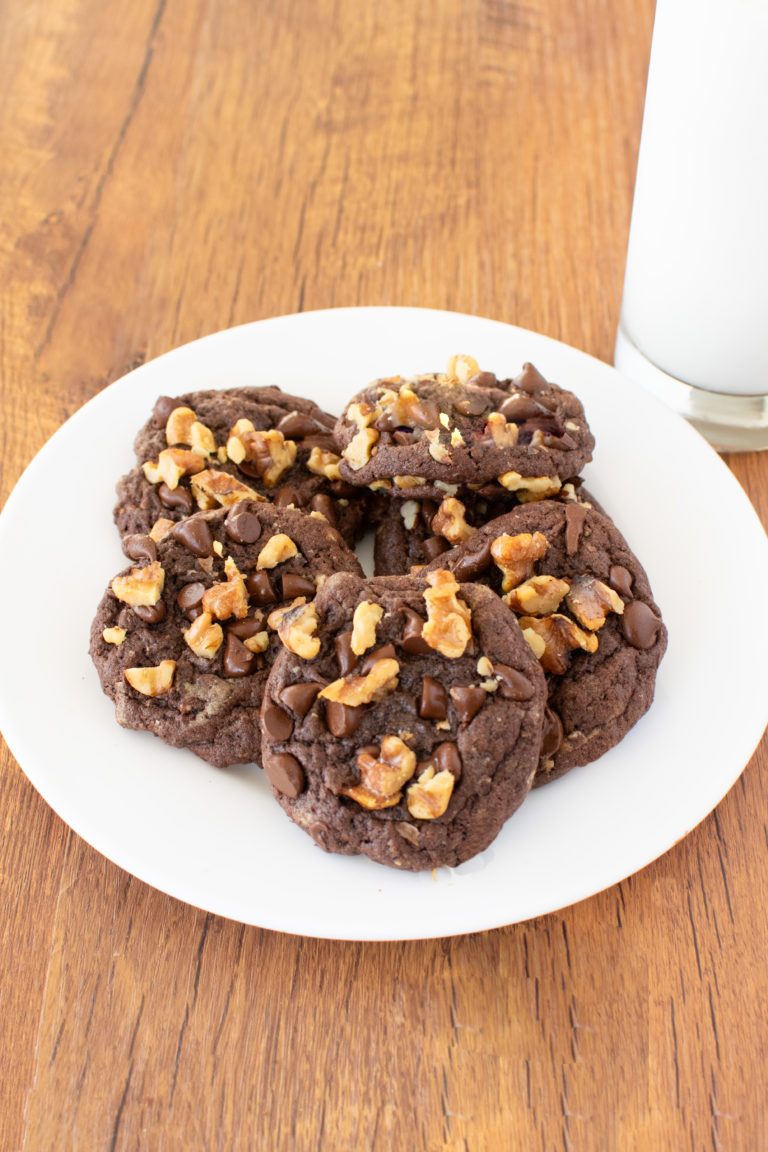 Easy Chocolate Chocolate Chip Walnut Cookies on a white plate by a clear glass of milk on a dark wood table