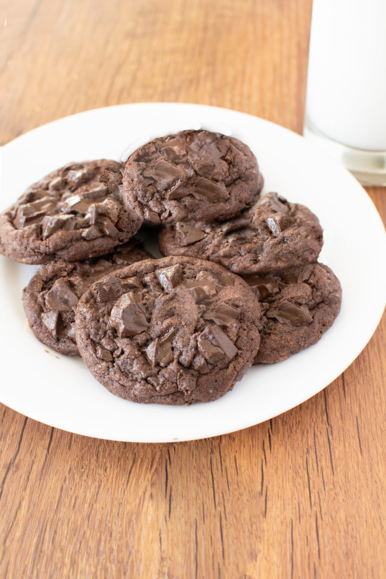 Easy Chocolate Chocolate Chunk Cookes on a white plate near a clear glass of milk on a dark wood table