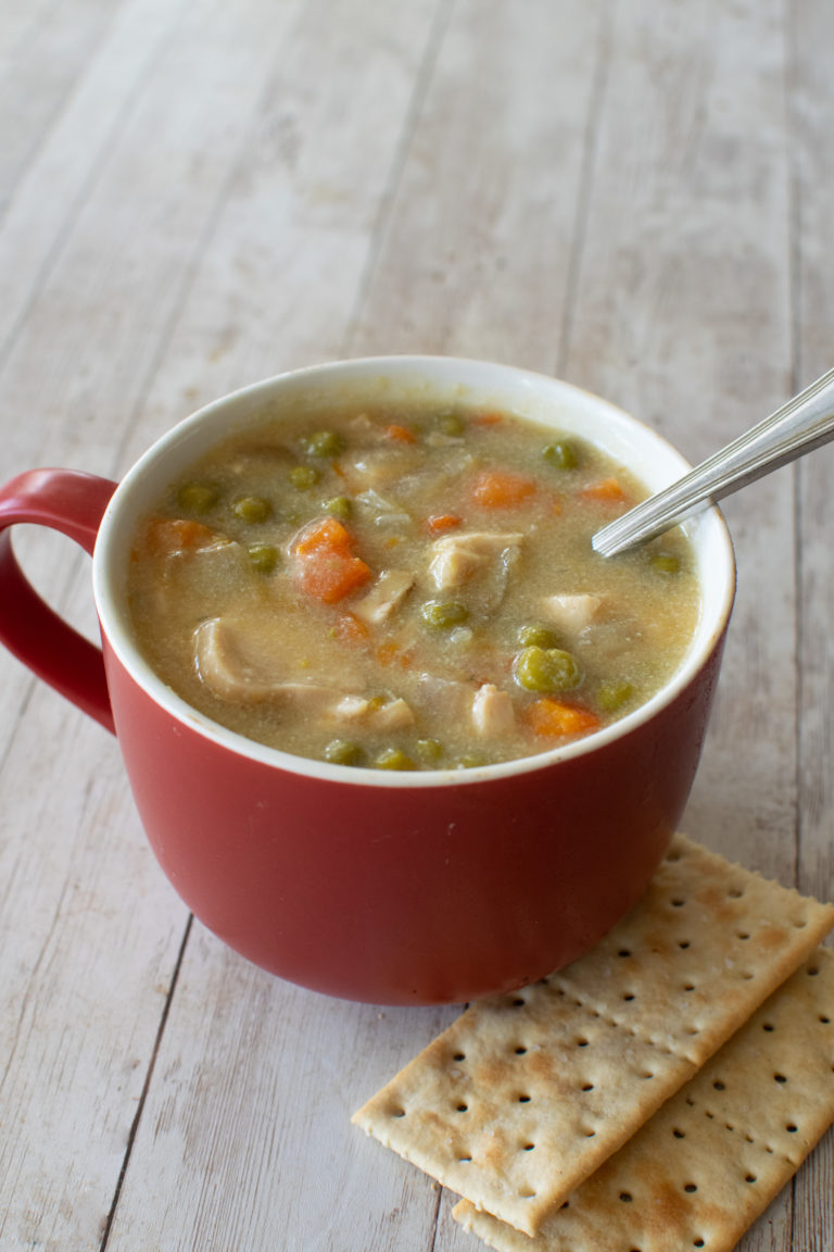 Easy Dairy-Free Chicken Pot Pie Soup in a red soup mug with a spoon near saltine crackers on a white wood table