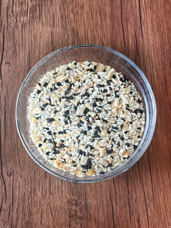 Everything Bagel Mix in a clear bowl on a dark wood table.