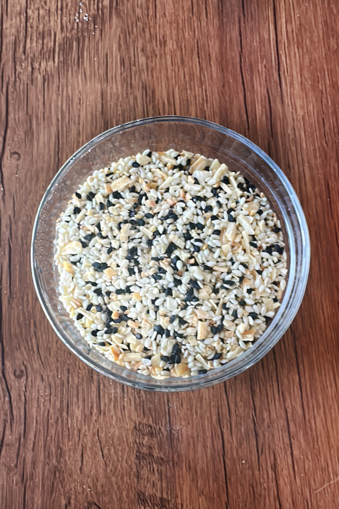 Homemade Everything Bagel Seasoning in a clear bowl on a dark wood table.