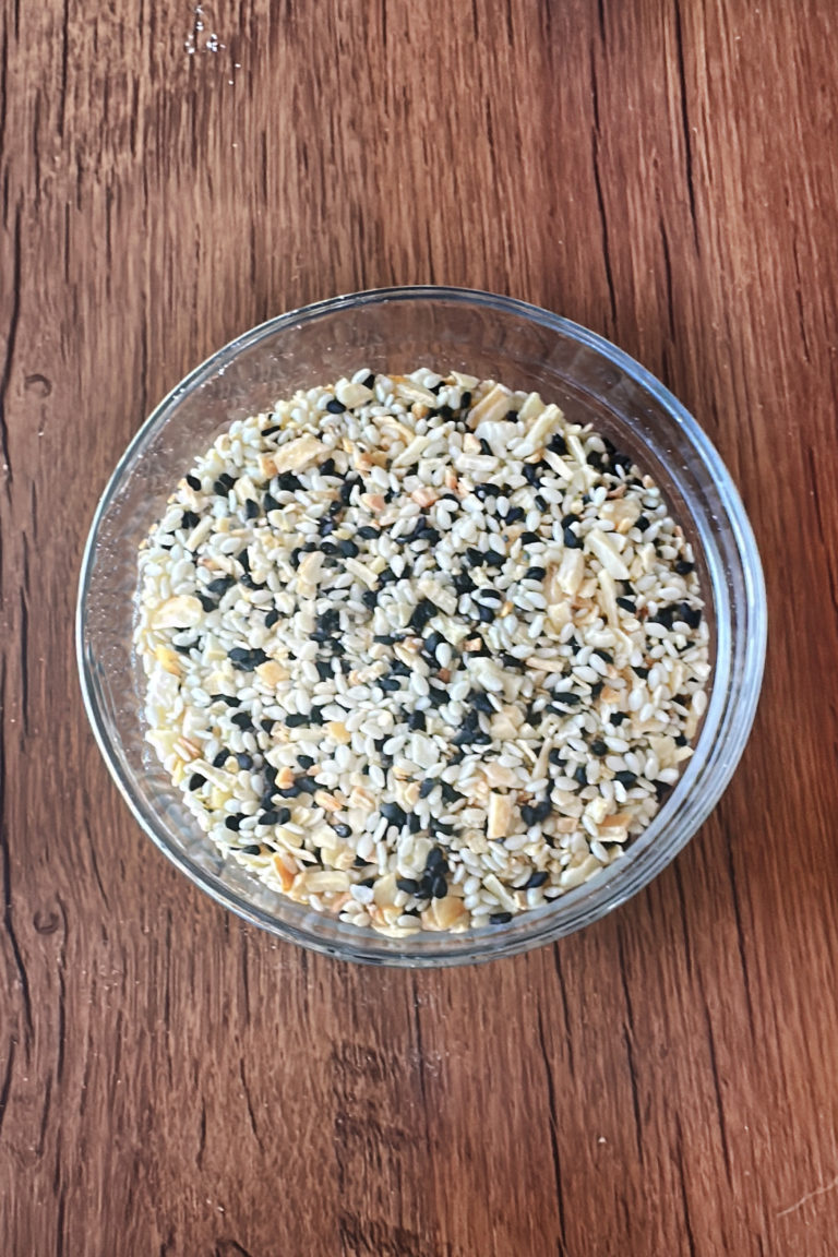 Everything Bagel Mix in a clear bowl on a dark wood table.