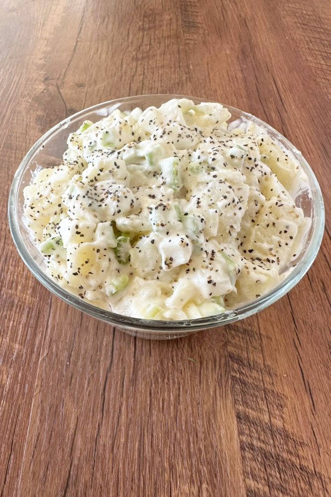 Hellman's potato salad in a clear bowl on a dark wood table.