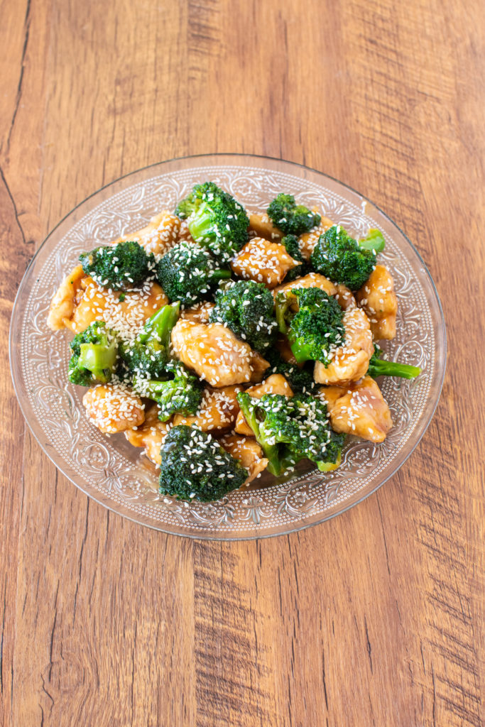 Honey Garlic chicken with broccoli in a clear serving bowl on a dark wood table