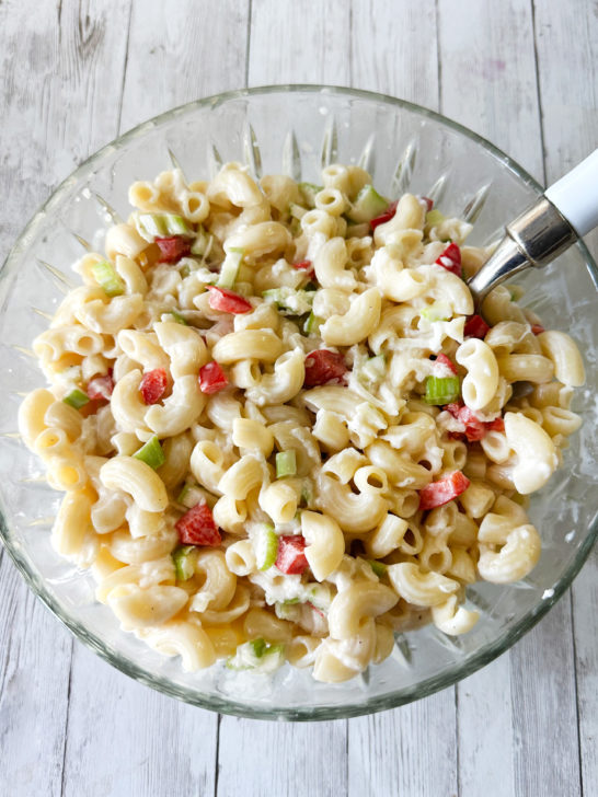 Deli-style macaroni salad in a clear bowl on a light wood table