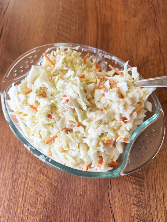deli coleslaw in a glass dish on a dark wood table.