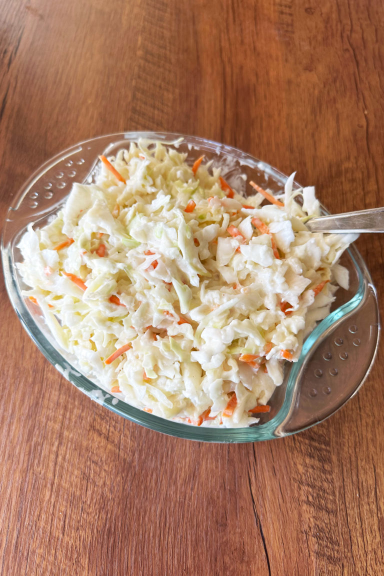 coleslaw in a glass dish on a dark wood table.