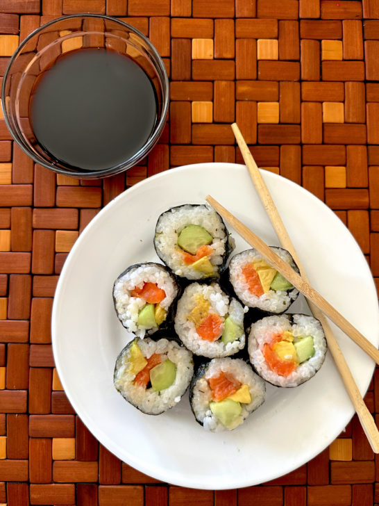 Easy Homemade sushi on a white plate with chopsticks next to a small bowl of soy sauce on a brown wooden background