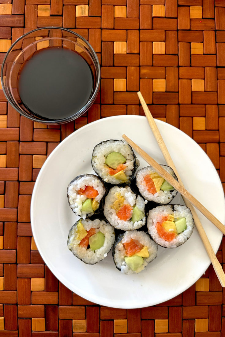 Easy Homemade sushi on a white plate with chopsticks next to a small bowl of soy sauce on a brown wooden background
