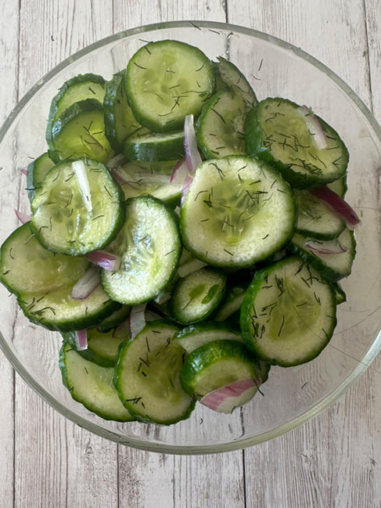 Deli-Style cucumber salad in a clear bowl on a white wood table