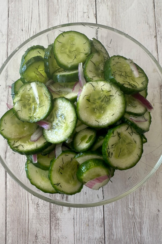 Deli-Style cucumber salad in a clear bowl on a white wood table