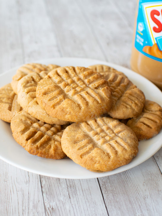 A pile of Dairy-free peanut butter cookies on a white plate on a while wood table.