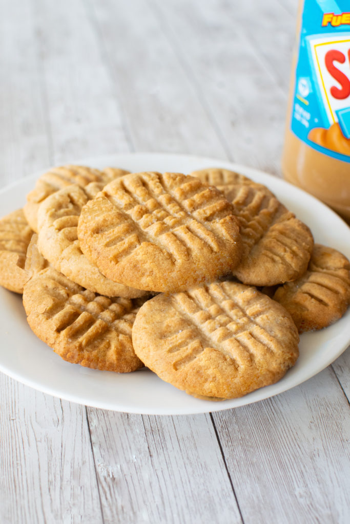 A pile of Dairy-free peanut butter cookies on a white plate on a while wood table.