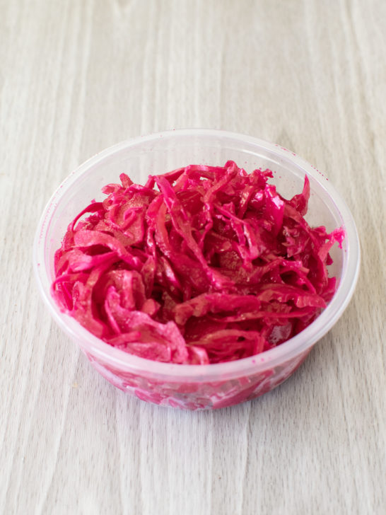 Container of sour red cabbage salad on a light wood table.