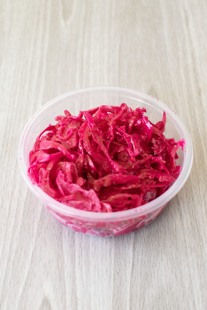 Container of sour red cabbage salad on a light wood table.
