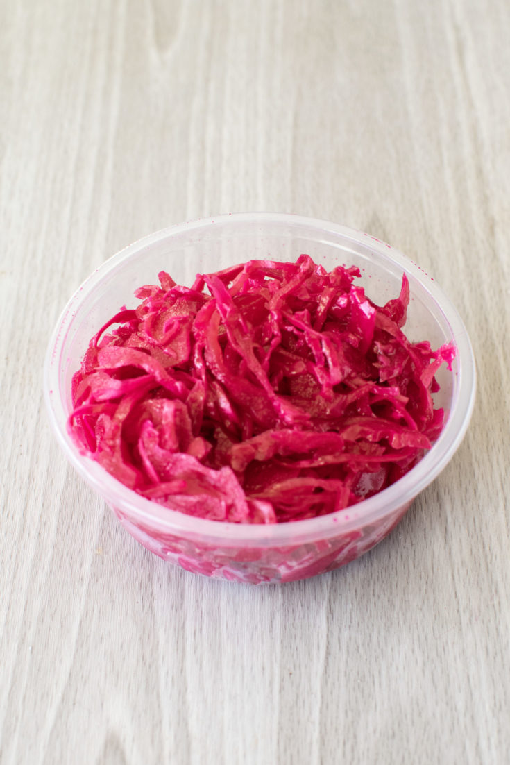 Container of sour red cabbage salad on a light wood table.