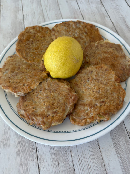 Fried tuna patties for passover on a plate around a lemon, all on a white wood background.