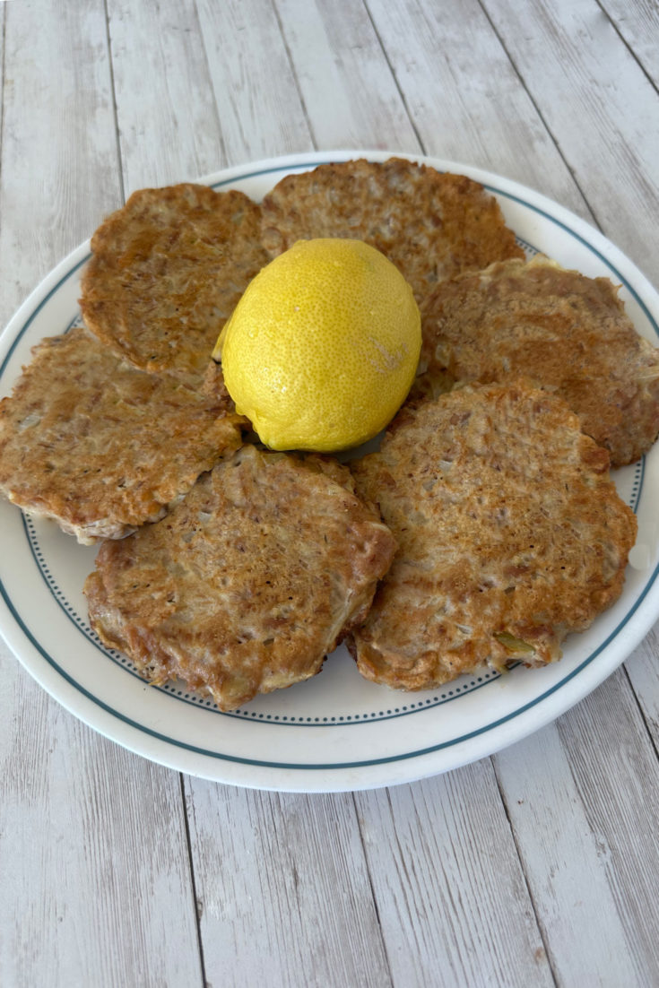 Fried tuna patties for passover on a plate around a lemon, all on a white wood background.