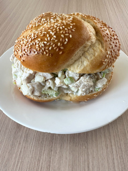 Deli Turkey Salad on a sesame seed roll on a white plate on a light wood table