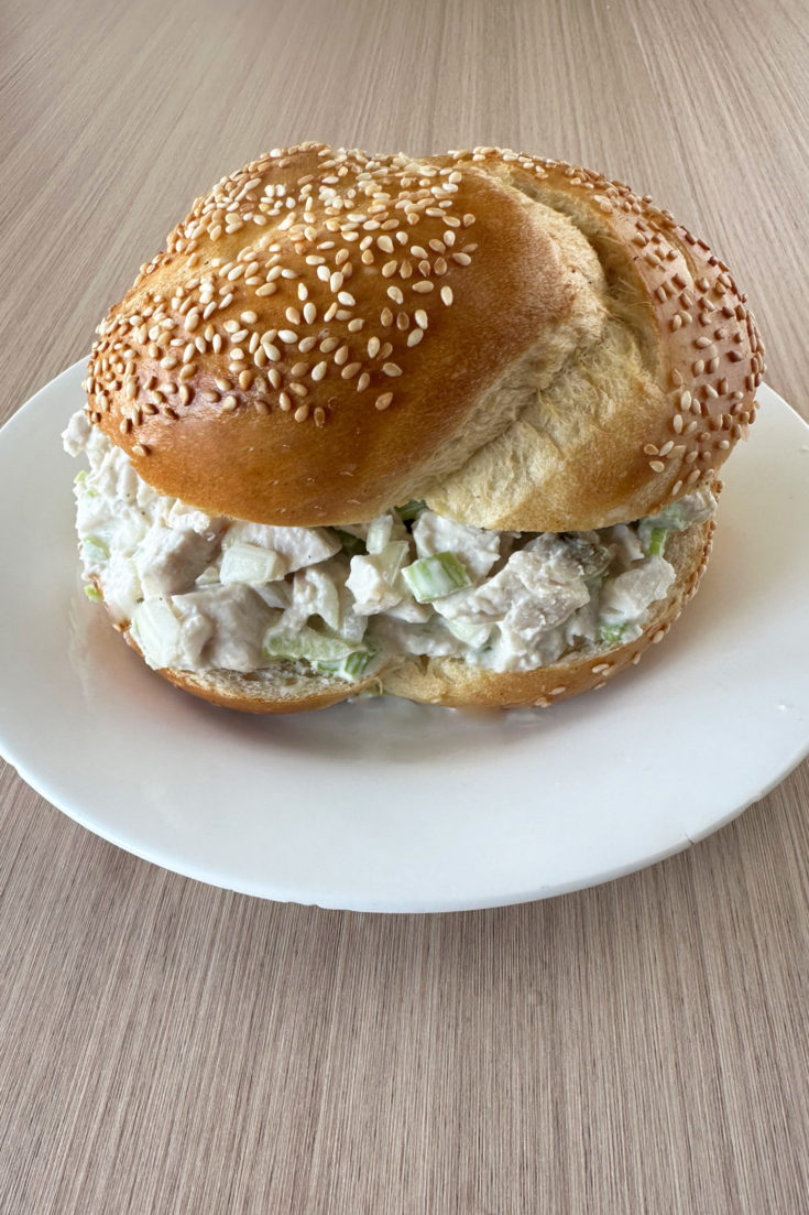 Deli Turkey Salad on a sesame seed roll on a white plate on a light wood table