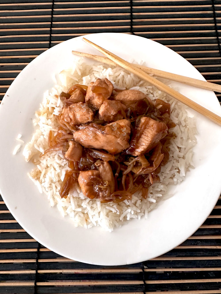 Kosher Chicken chop suey on a bed of white rice on a white plate with chopsticks on a dark brown bamboo mat.